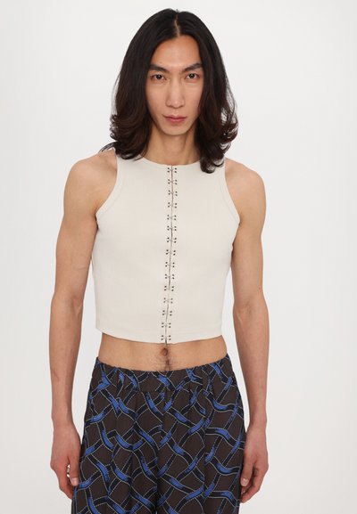 Crop top blanc à rayures avec un col rond et un détail de bouton central. Associé à un pantalon noir ample à motifs avec des accents bleus.