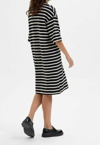 Robe rayée noir et blanc avec des manches courtes, coupe ample, fentes latérales et longueur genou. Associée à des chaussures noires brillantes.