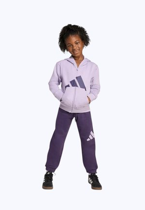 Sudadera con capucha morada con un gran logo en tono púrpura oscuro y pantalones deportivos morados a juego con un logo similar, combinados con zapatillas negras.
