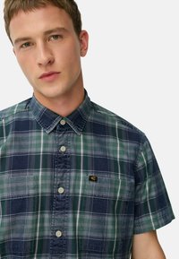 Polo met korte mouwen in groen en marineblauw, gemaakt van katoen. Bevat een button-down kraag, voorkruisen en een klein logo op de borst.