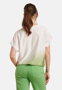 Short-sleeve blouse featuring a gradient from white to green, made of smooth fabric. Paired with fitted green pants with back pockets.