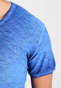 Niebieska koszulka z dekoltem w kształcie litery V, charakteryzująca się gradientem od jasnoniebieskiego do ciemnoniebieskiego, uszyta z miękkiej bawełny o delikatnej teksturze i z haftowanym detalem kieszonki.