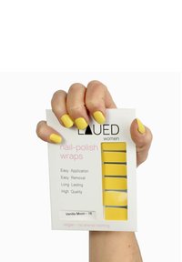 Gelbe Nagellackfolien werden in einer Hand gehalten. Die Verpackung ist weiß mit pinkfarbener Schrift und zeigt sieben gelbe Folien darin. Auffällig für die einfache Anwendung.