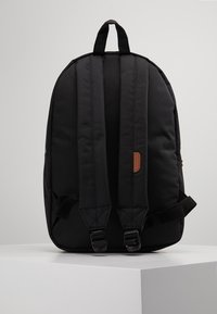 Zwarte stoffen rugzak met verstelbare, gevoerde bandjes, een bovenhandgreep en een tankleurige leren accenten. Heeft een gestroomlijnde vorm en een minimalistisch ontwerp.