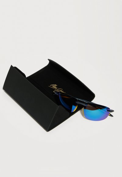 Μαύρα γυαλιά ηλίου με μπλε αντανακλαστικούς φακούς που ακουμπούν σε μια ανοιχτή μαύρη θήκη με την επωνυμία Maui Jim, πάνω σε λευκή επιφάνεια.