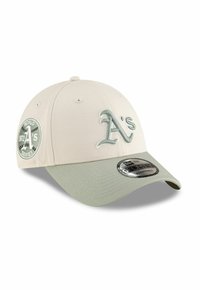 Gorra de béisbol beige con visera verde. Presenta el logo de "A's" y un parche que dice "Serie Mundial 1972" con acentos de costura. Con correa ajustable en la parte posterior.
