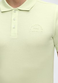 Ανοιχτό πράσινο πόλο μπλουζάκι με τρία λευκά κουμπιά και κεντημένο κείμενο "KARL LAGERFELD PARIS 21 RUE ST-GUILLAUME" στο στήθος.