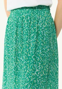 Jupe verte à motifs avec une taille élastique, ornée de formes abstraites blanches et jaunes sur un fond vert, texture lisse.
