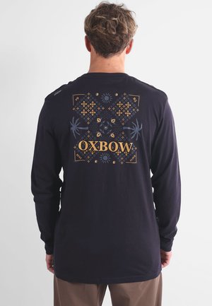 T-shirt à manches longues sombre avec un design géométrique coloré et le texte "OXBOW" au dos. En coton, avec une coupe décontractée.
