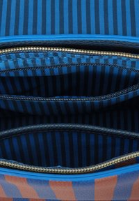 Das Innenleben der Reißverschlussstofftasche weist drei Fächer auf, die mit dunkelblauem und schwarzem gestreiftem Material ausgekleidet sind; sichtbare goldene Hardwareakzente.