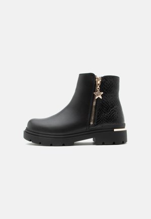 Bottine noire à la cheville avec dos texturé, fermeture éclair dorée décorative et breloque étoile, semelle épaisse en caoutchouc et petit talon.