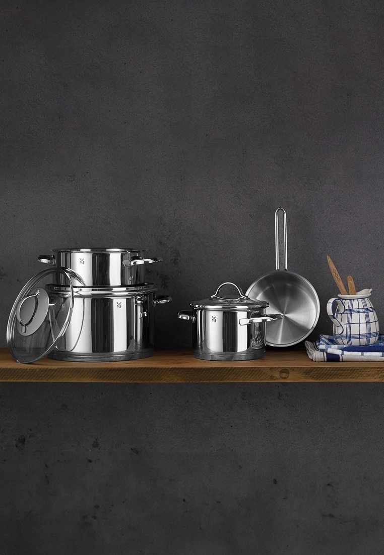 Ensemble de casseroles en acier inoxydable sur une étagère en bois, présentant des surfaces polies, des couvercles en verre et une louche assortie, sur fond sombre.