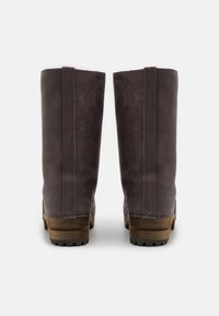 Bruna läderknähöga stövlar med en slät textur, tydlig kontrasterande sömnad, staplad träklack och gummisålar för bra grepp.