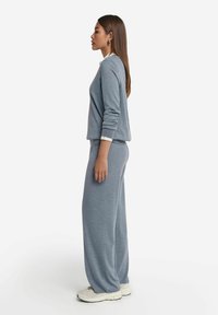 Grå avslappnad sweatshirt i passform och matchande vida byxor i mjukt material, med en subtil struktur och elastiska ärmmuddar. Avslutade med neutrala sneakers.