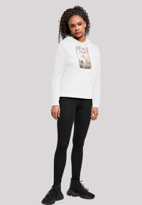 Felpa bianca con stampa grafica, tasca frontale e polsini a costine, abbinata a leggings neri e scarpe nere. Tessuto dalla consistenza liscia.