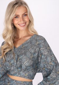 Top cropped grigio a fantasia con scollo a V, maniche lunghe a sbuffo e intricati disegni di foglie con accenti blu e gialli.