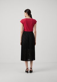 Red fitted t-shirt with short sleeves, paired with a black pleated midi skirt. The skirt features a waistband and smooth texture.