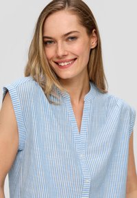 Lichtblauw gestreepte blouse met een V-hals, korte mouwen en knoopdetails. Gemaakt van een zachte stof met een gladde textuur.