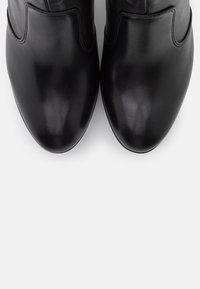 Botines de cuero negro con una textura suave, punta redondeada y un detalle de costura mínimo. Presentan un diseño elegante y ajustado.