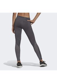 Leggings atletici grigi con pannelli in rete, design aderente e vita alta, abbinati a scarpe da corsa nere.