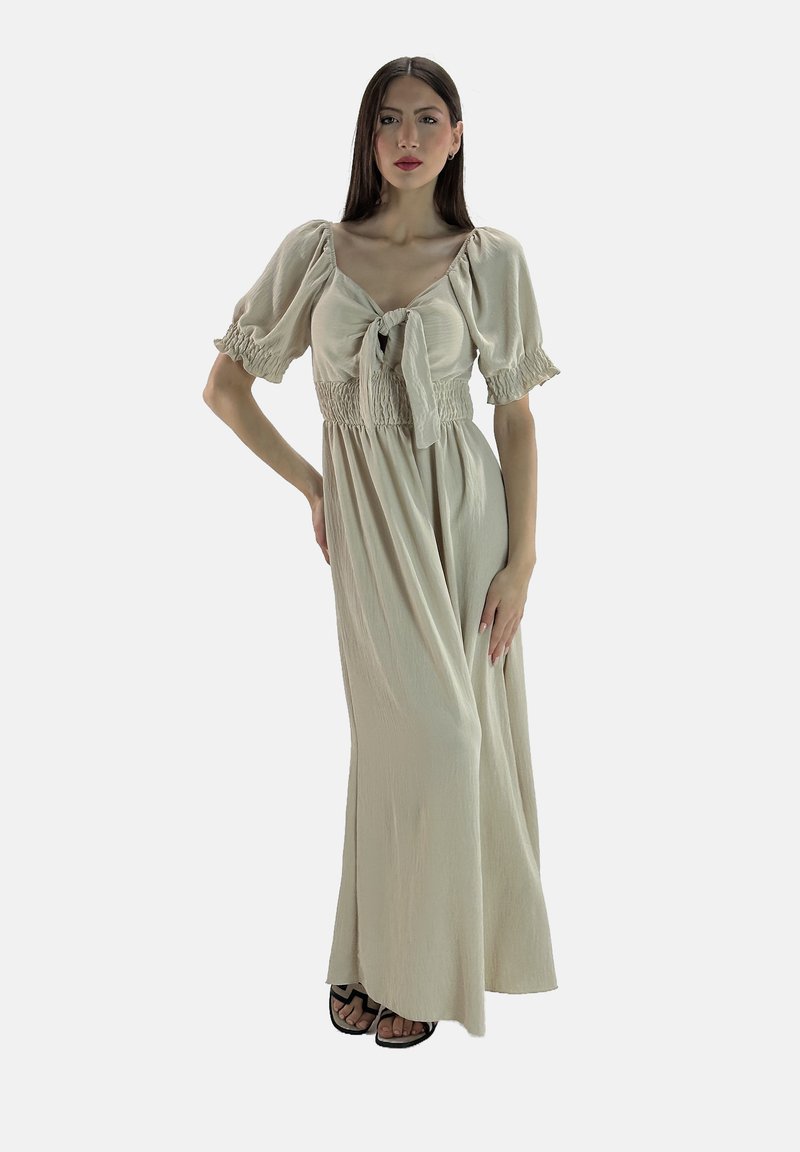 Abito lungo beige con maniche a palloncino e dettaglio di laccio davanti. Il corpino presenta un design arricciato, scendendo verso una gonna ampia. Indossato con sandali neri.