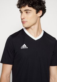 Svart sportströja med V-halsdesign, korta ärmar och vita detaljer. Adidas-logga broderad på vänster bröst. Slät textur.