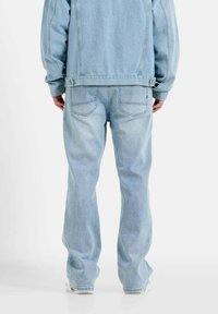 Chaqueta y pantalones de mezclilla de color azul claro, con un corte relajado, costuras visibles y dos bolsillos traseros con una textura ligeramente desgastada.