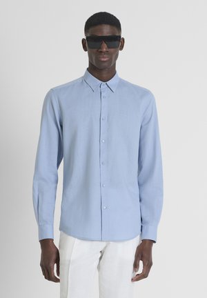 Himmelblaue, langärmlige Druckknopf-Bluse aus weichem Stoff, mit klassischem Kragen und Knopfverschlüssen, kombiniert mit schwarzen Sonnenbrillen.