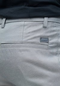 Κοντινή λήψη ανοιχτό γκρι παντελονιού με οριζόντια πίσω τσέπη και ραμμένη ορθογώνια ετικέτα με το λογότυπο στη δεξιά πλευρά.