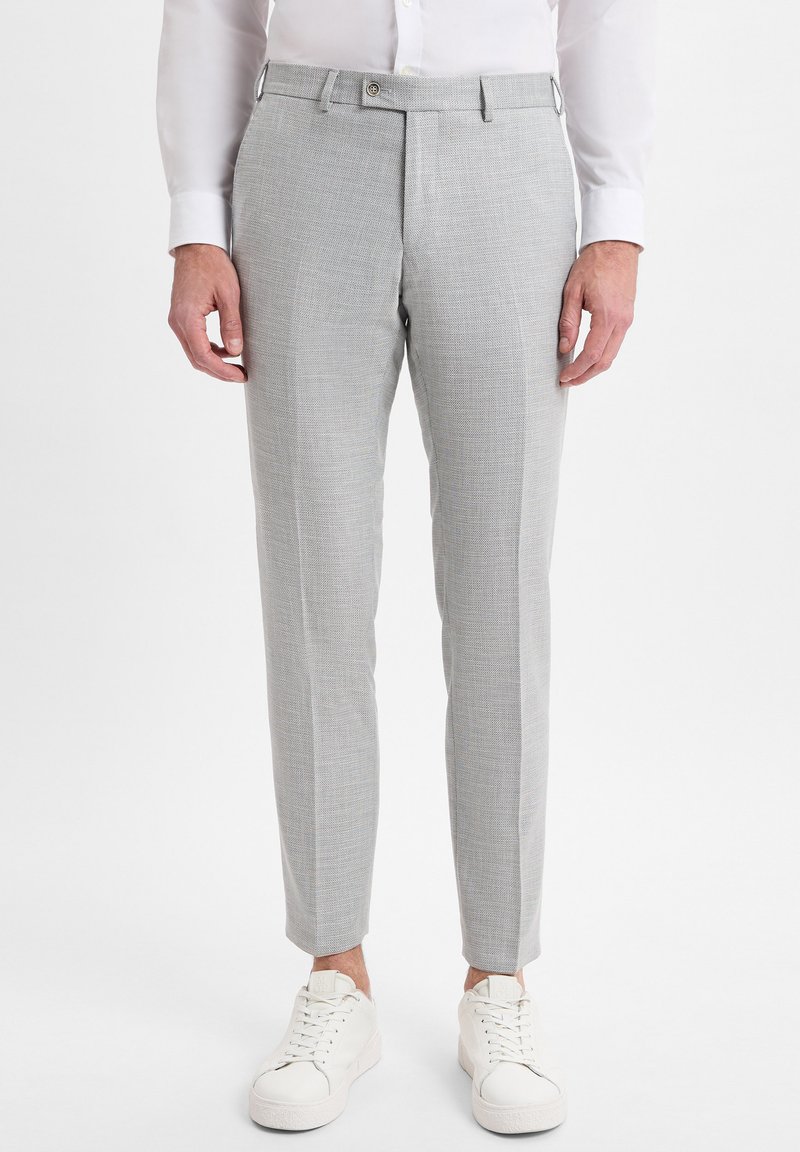 Hellgraue, maßgeschneiderte Hose aus strukturiertem Stoff mit flachem Bund, seitlichen Taschen und schlanker Passform, kombiniert mit weißen Sneakers.