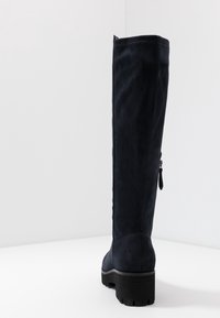 Botte en daim bleu marine hauteur genou avec un bout arrondi, un matériau texturé et une semelle épaisse en caoutchouc noir. Dispose d'une fermeture éclair latérale.