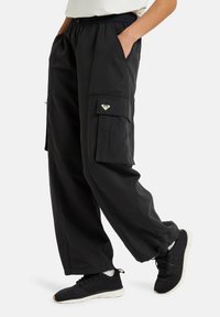 Black cargo pants with an elastic waistband, side pockets, and an accent pocket featuring a small logo. Made from a smooth, lightweight material.