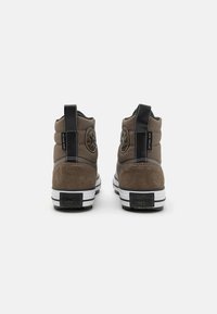 Sneakers înalte din sueded maro, cu accente din piele neagră, având un detaliu al logo-ului pe lateral, o talpă intermediară albă și o talpă exterioară cu dungi negre și albe.