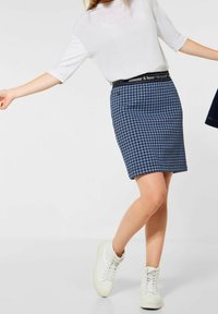 Modrá sukně na tužku s houndstooth vzorem a kontrastním černým elastickým pasem se textem. V kombinaci s bílými vysokými teniskami a bílým topem.