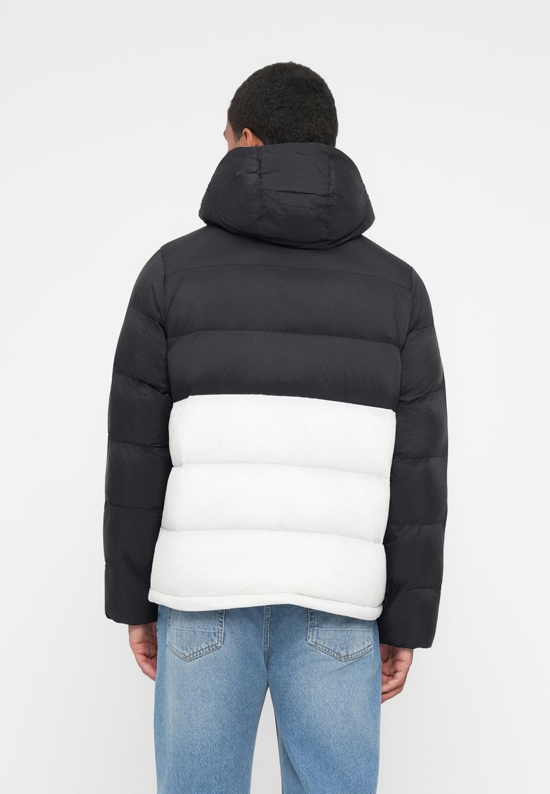 Daunenjacke mit schwarzem oberen Teil und weißem mittleren Teil. Verfügt über eine Kapuze, ein horizontal gequiltetes Muster und elastische Bündchen.