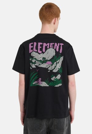 Osoba z rudymi włosami w czarnej koszulce z kolorowym wzorem gór, roślin, namiotu oraz napisem "ELEMENT" na plecach.