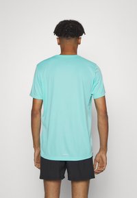 Světlá akvamarínová sportovní tričko s krátkým rukávem vyrobené z hladké tkaniny s kulatým výstřihem; nošené s tmavými šortkami, které mají na lemu decentní logo.