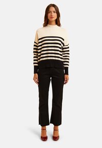 Maglione a maglia con strisce orizzontali crema e nere, collo alto, vestibilità ampia, abbinato a pantaloni neri a vita alta e tacchi rossi a punta chiusa.