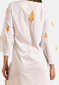 Robe en coton blanche à manches trois-quarts, ornée d'accents de broderie florale jaune sur les manches et le dos. Tissu doux et léger.
