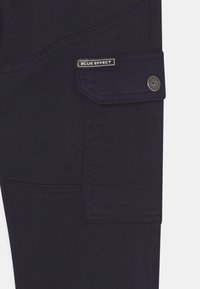 Námořnické cargo kalhoty s klopovou kapsou a kovovým patentem a štítkem "BLUE EFFECT", vyrobené z odolné tkaniny s hladkým povrchem.