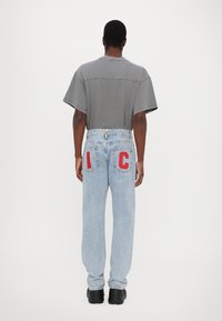 Tricou gri cu mânecă scurtă, asociat cu blugi din denim de un albastru deschis, cu croială largă, având brodare roșie "I C" pe buzunarele din spate. Se remarcă o pereche de pantofi negri.