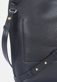 Sac en cuir noir grainé avec une surface texturée, doté d'une poche plaquée et d'accents de quincaillerie dorée sur la sangle.
