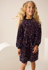 Robe noire ornée de sequins avec des embellissements colorés et brillants. Manches longues avec des poignets noirs. Coupe ample, longueur genou. Texture lisse.