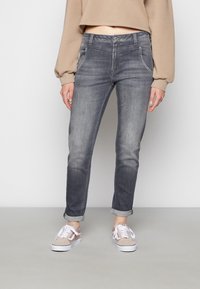 Jeans de mezclilla gris con un corte ajustado, desvanecimiento sutil, trabillas para cinturón y puños enrollados, combinados con zapatillas gris claro.