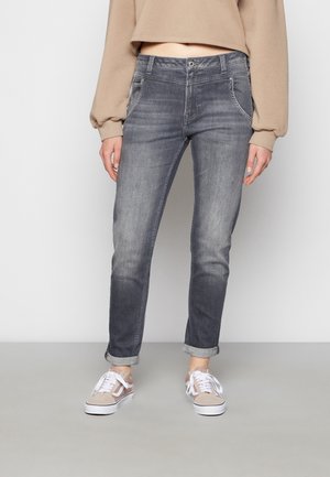 Jeans de mezclilla gris con un corte ajustado, desvanecimiento sutil, trabillas para cinturón y puños enrollados, combinados con zapatillas gris claro.