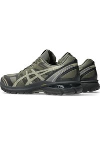 Dunkelgrüne Laufschuhe mit einer strukturierten Oberseite, die ein Wellenmuster und schwarze Akzente aufweist. Leichte Sohle mit sichtbarer Dämpfungstechnologie.