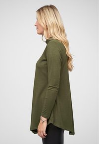 Haut à manches longues vert olive avec un col haut, présentant une coupe confortable et un ourlet arrière légèrement plus long. Matière douce et texturée.