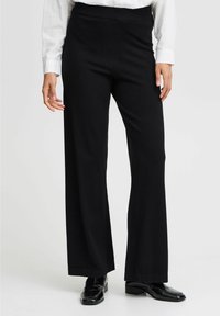 Zwarte broek met wijde pijpen van een zachte stof, een elastische tailleband en een nette afwerking aan de zoom, gecombineerd met glanzende zwarte schoenen.