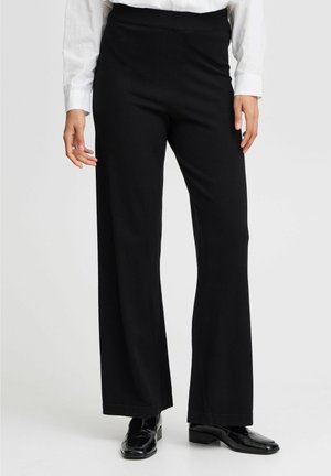 Zwarte broek met wijde pijpen van een zachte stof, een elastische tailleband en een nette afwerking aan de zoom, gecombineerd met glanzende zwarte schoenen.