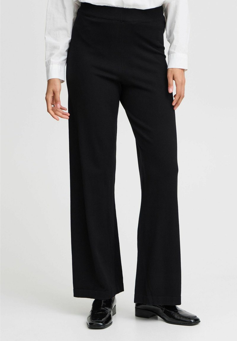 Zwarte broek met wijde pijpen van een zachte stof, een elastische tailleband en een nette afwerking aan de zoom, gecombineerd met glanzende zwarte schoenen.